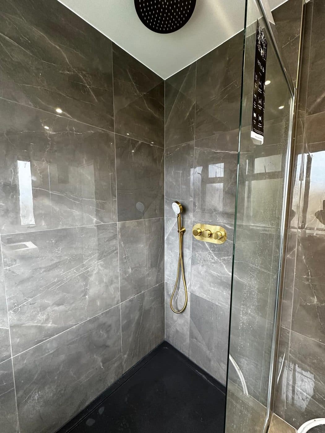 Grey marble-effect walk-in wet room with gold brassware and rainfall shower, tiled and fitted in London by ERCO Home Improvements